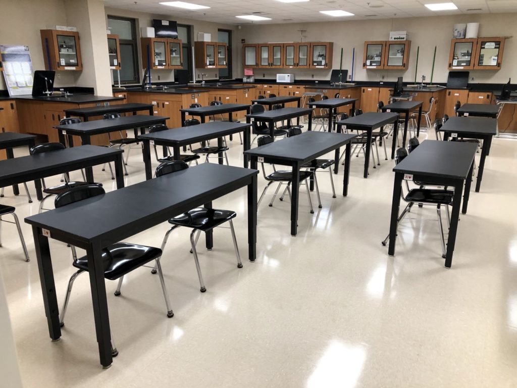 School science classroom with a cream speckled VCT tile floor finished to an even sheen, black lab tables and stools set out across it
