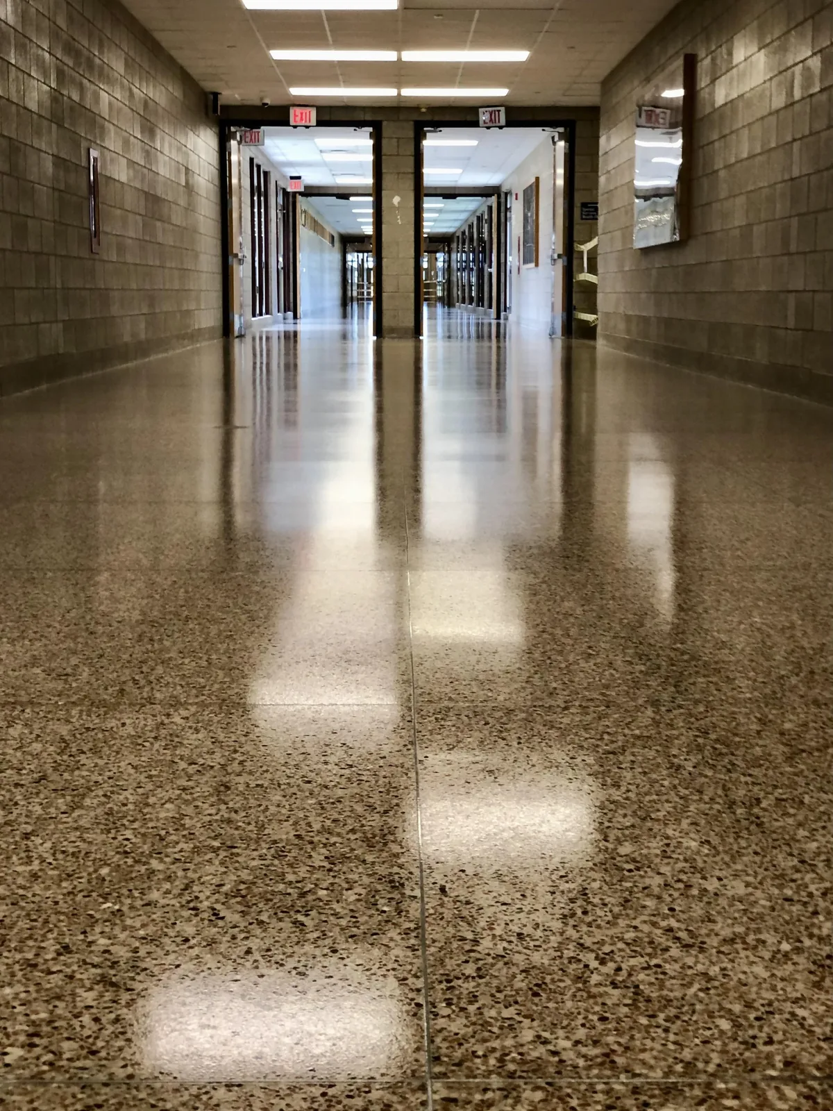 School corridor with a speckled VCT tile floor coated to a mirror finish, reflecting the ceiling lights down its length