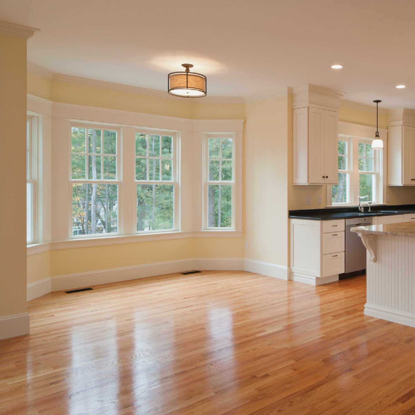 Open-plan dining area in pale blond narrow-strip oak with a high-gloss finish, curved bay window and cream kitchen cabinets beyond