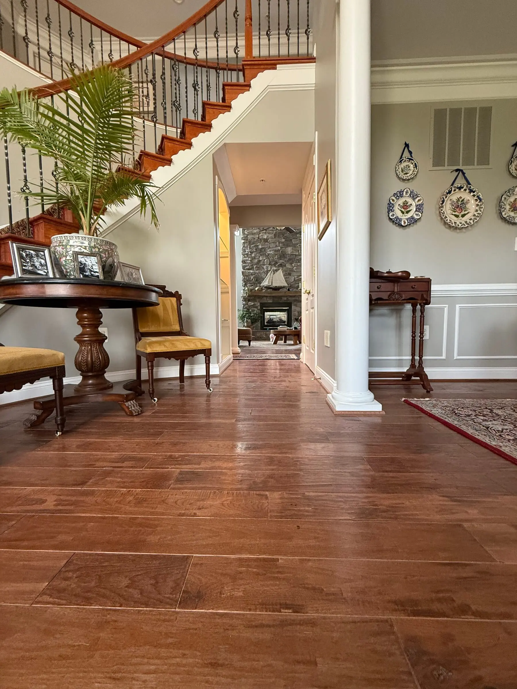Two-storey entry hall with wide reddish-brown hardwood planks in a satin finish, a curved staircase with iron balusters rising to the left
